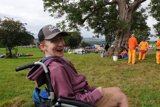 A young man in a wheelchair wearing a baseball cap and smiling