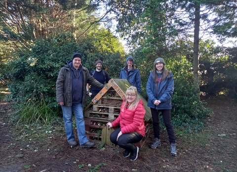 5 people standing around a bug hotel in a woodland