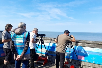 Two men are using telescopes looking out to see across Morecambe Bay from the top of Rossall Point Observation Tower.