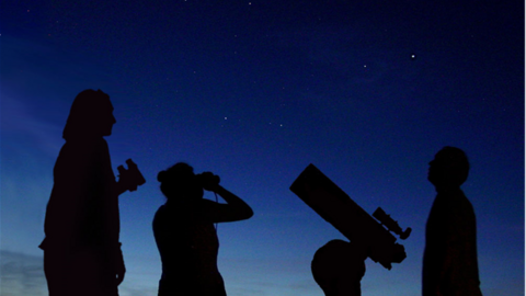 Three people stargazing at dusk.