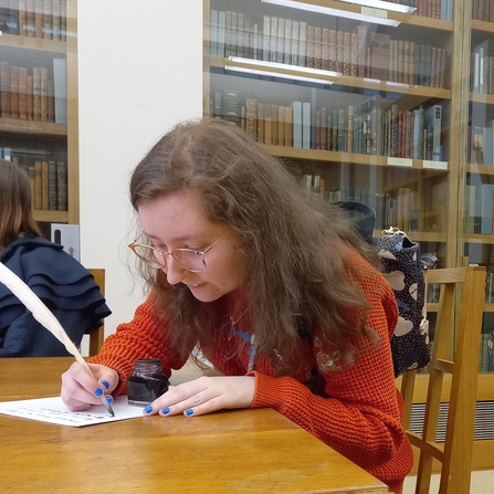 A young woman writing with a quill in a library