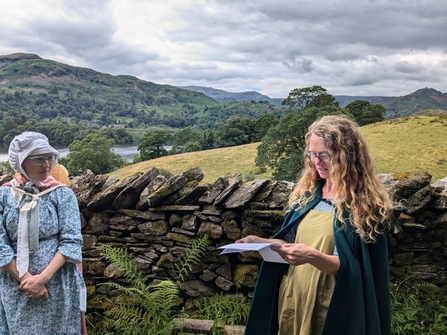 People in cloaks reading poetry in front of a dry stone wall